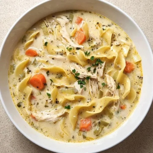 A bowl of creamy chicken noodle soup with vegetables and herbs